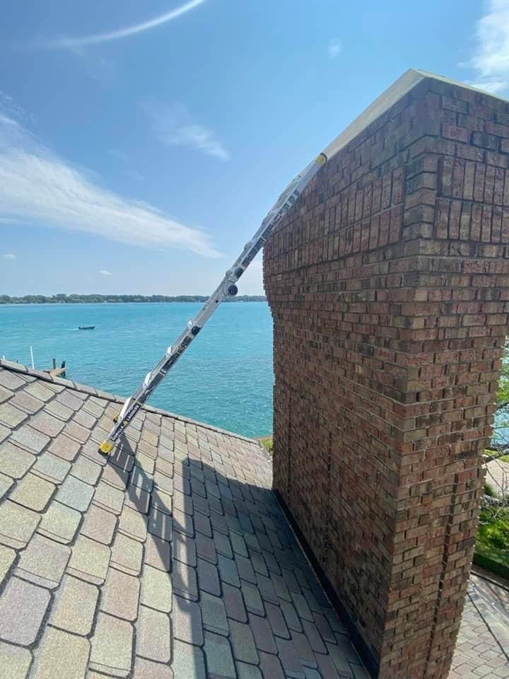 A ladder is leaning against a brick chimney on a roof overlooking the ocean.