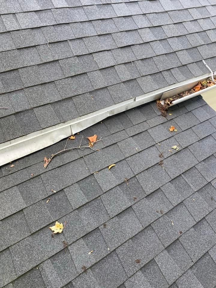 A close up of a gutter on a roof with leaves on it.