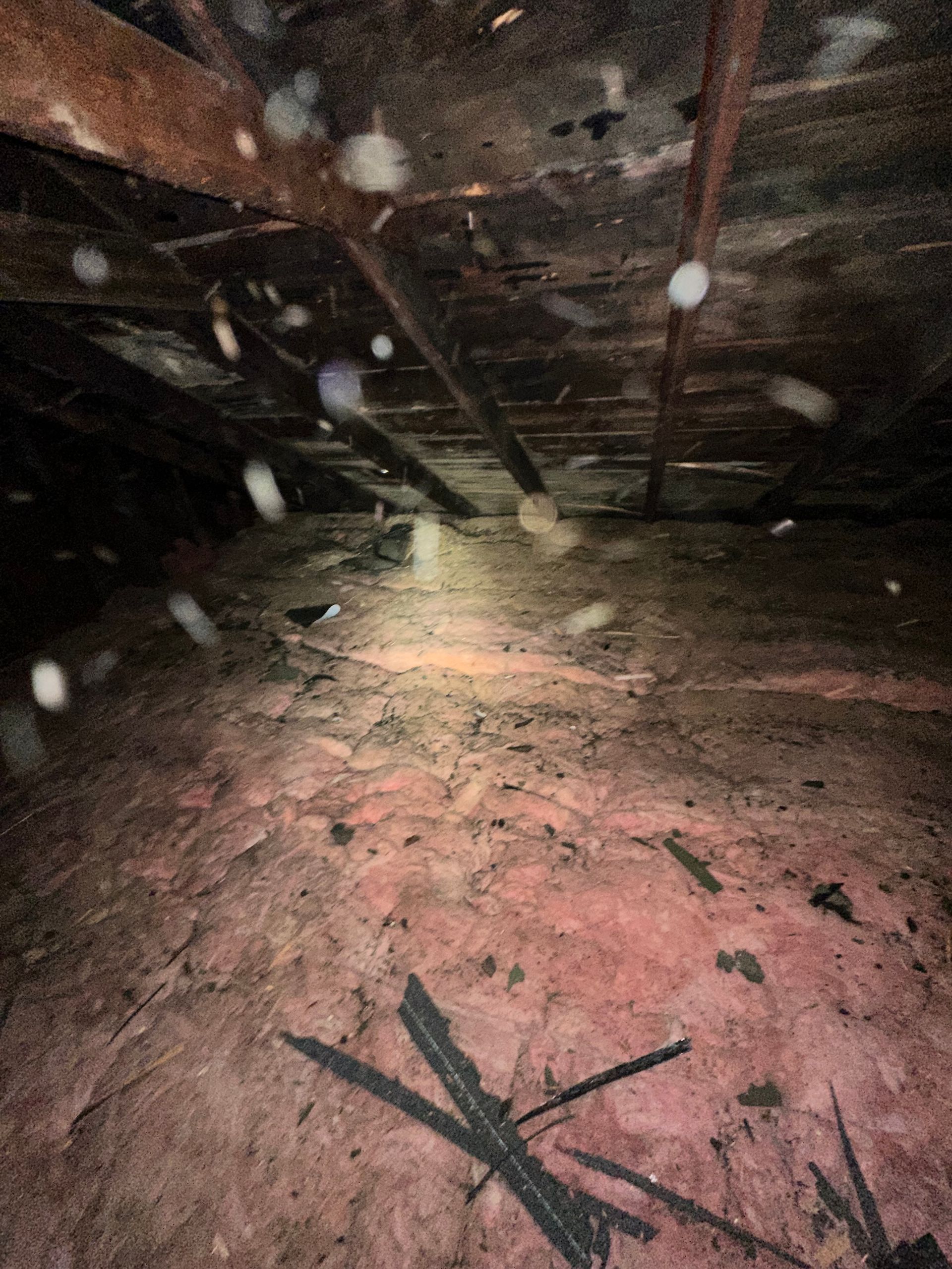 A dark attic with a lot of dust on the floor and ceiling.