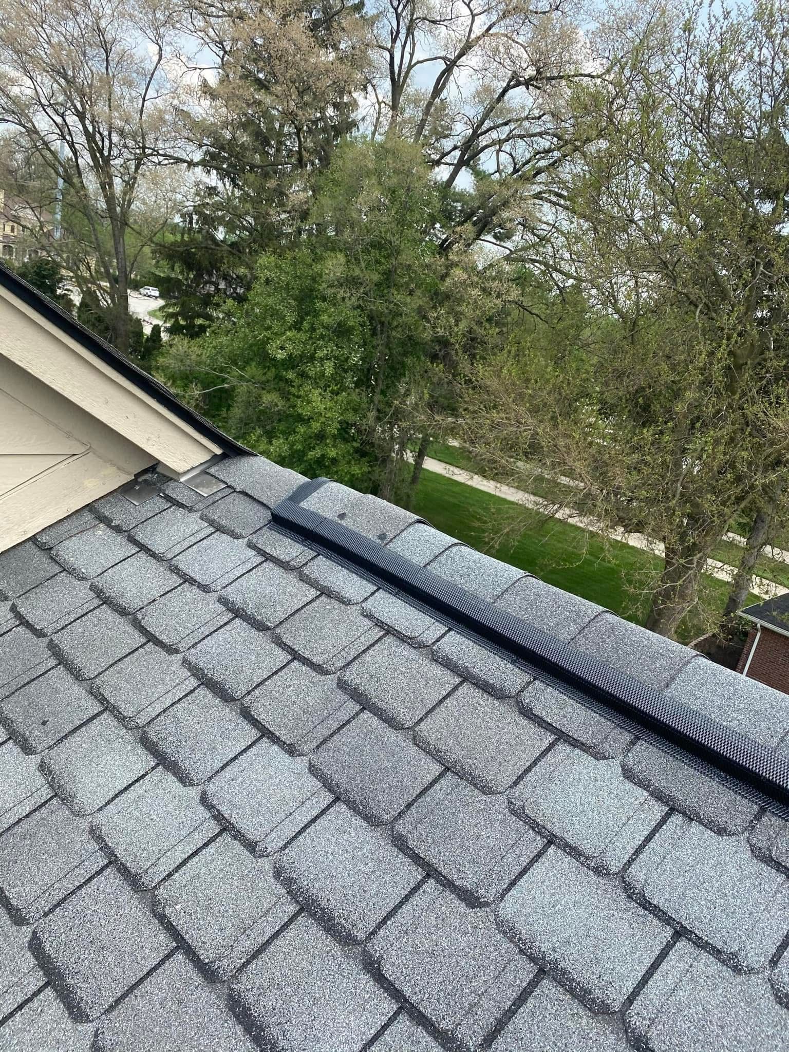 A close up of a roof with shingles and trees in the background.