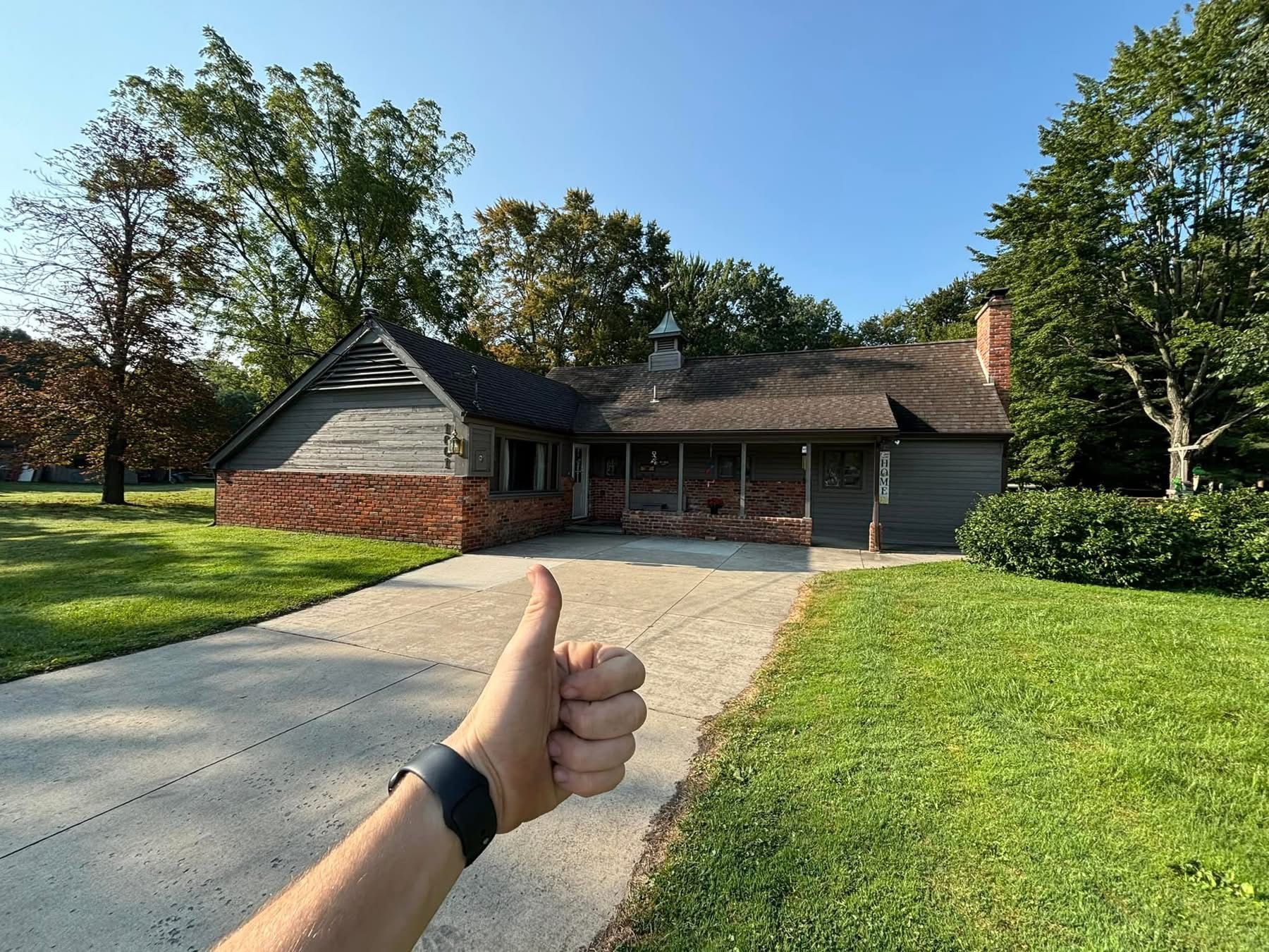 A person is giving a thumbs up in front of a house