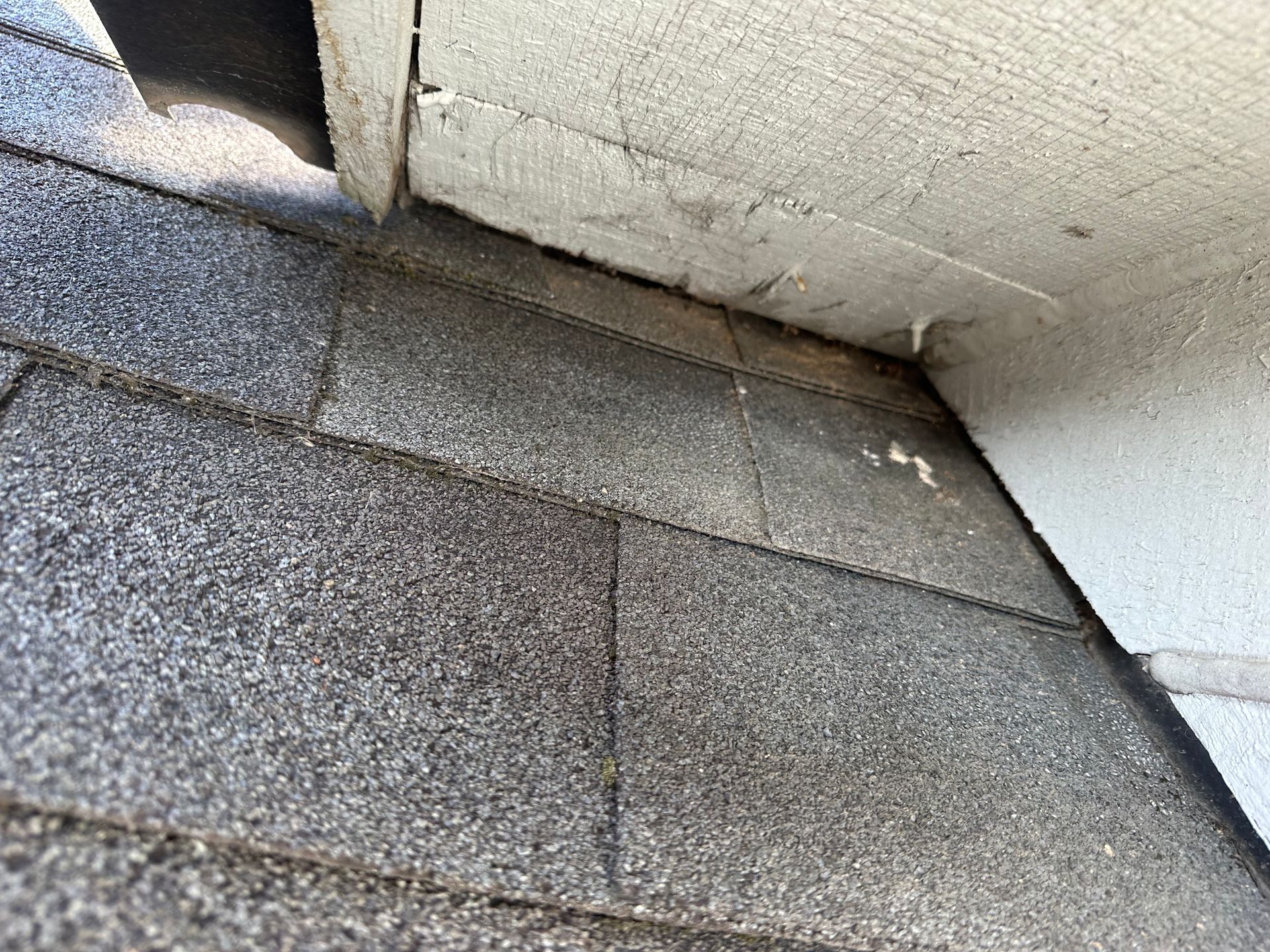 A close up of a roof with shingles and a white wall.