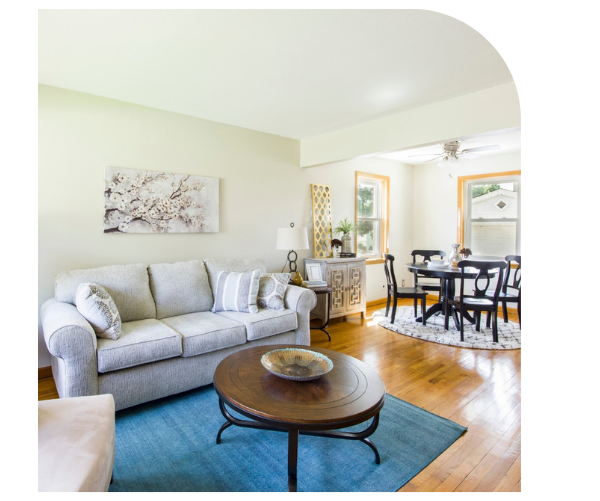 Bright living room with gray sofa, blue rug, round coffee table, and dining area in the background