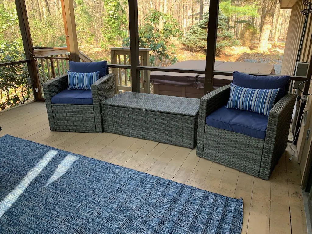 A screened in porch with wicker furniture and a blue rug.