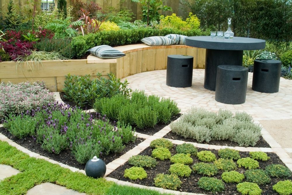 Modern garden patio with round black table, stools, and geometric flower beds