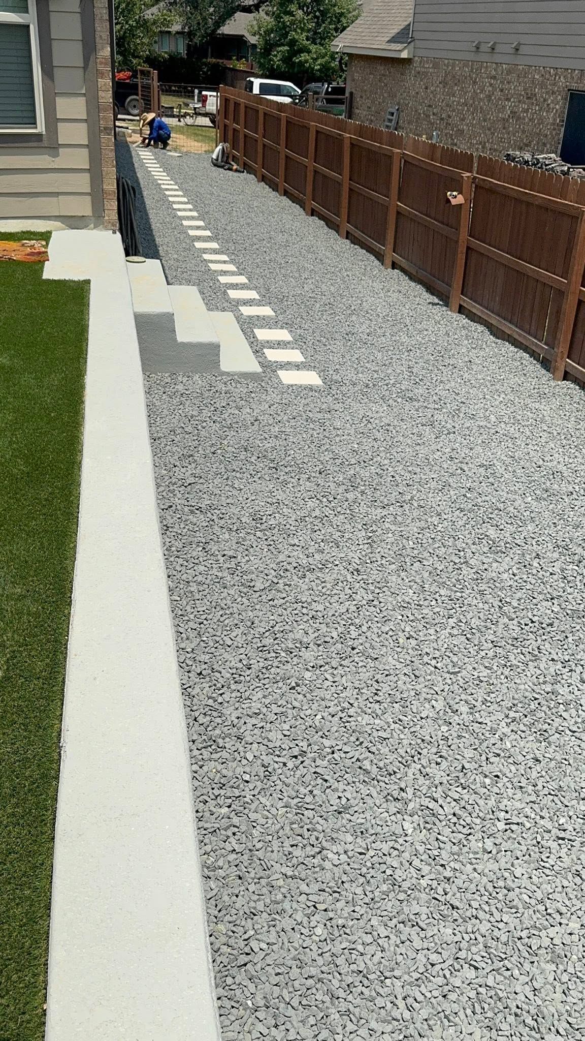 Gravel side yard with concrete edging, stepping stones, and a wooden fence alongside a house.