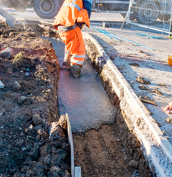 A construction worker is pouring concrete into a trench