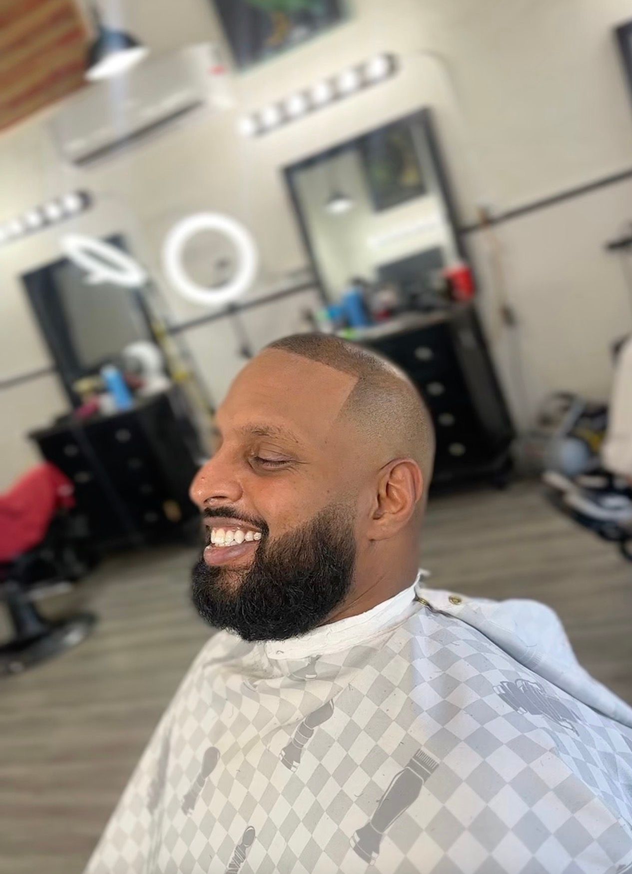 Man with a short haircut and full beard smiles at a barber shop.