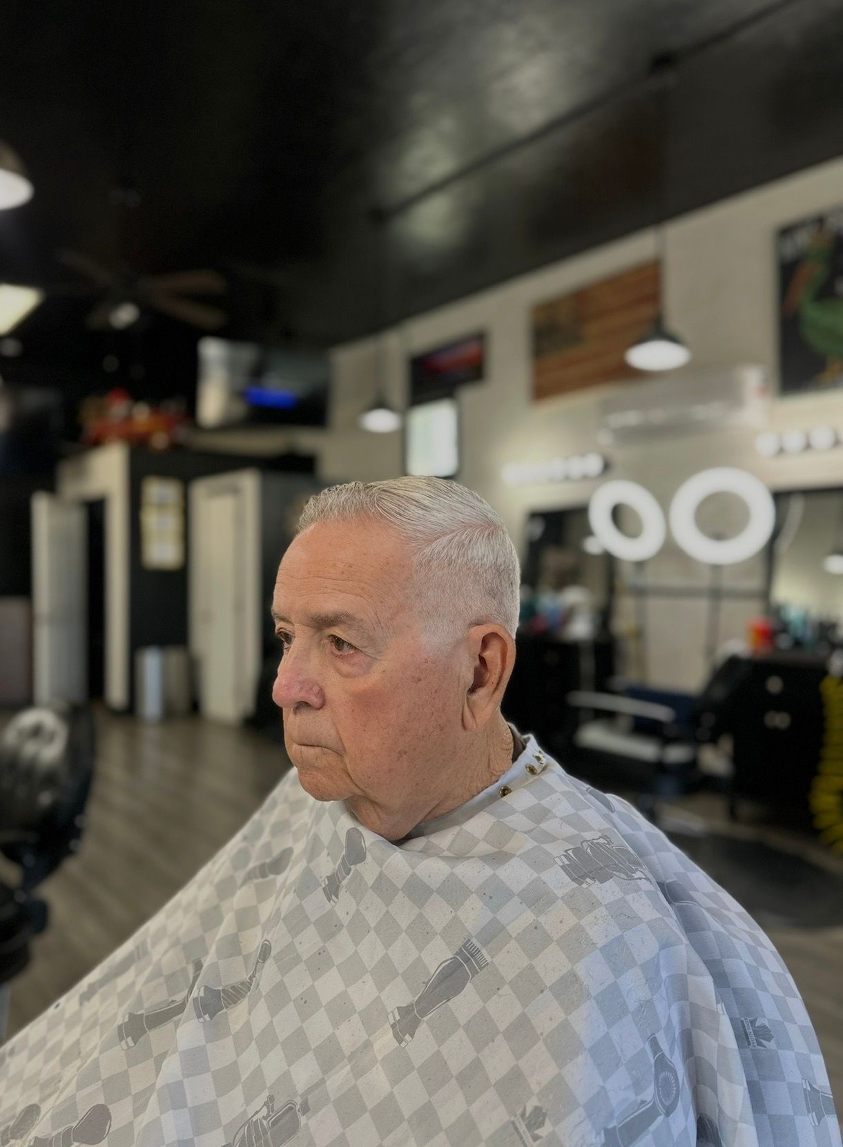 Man with a short haircut in a barber shop, wearing a cape.