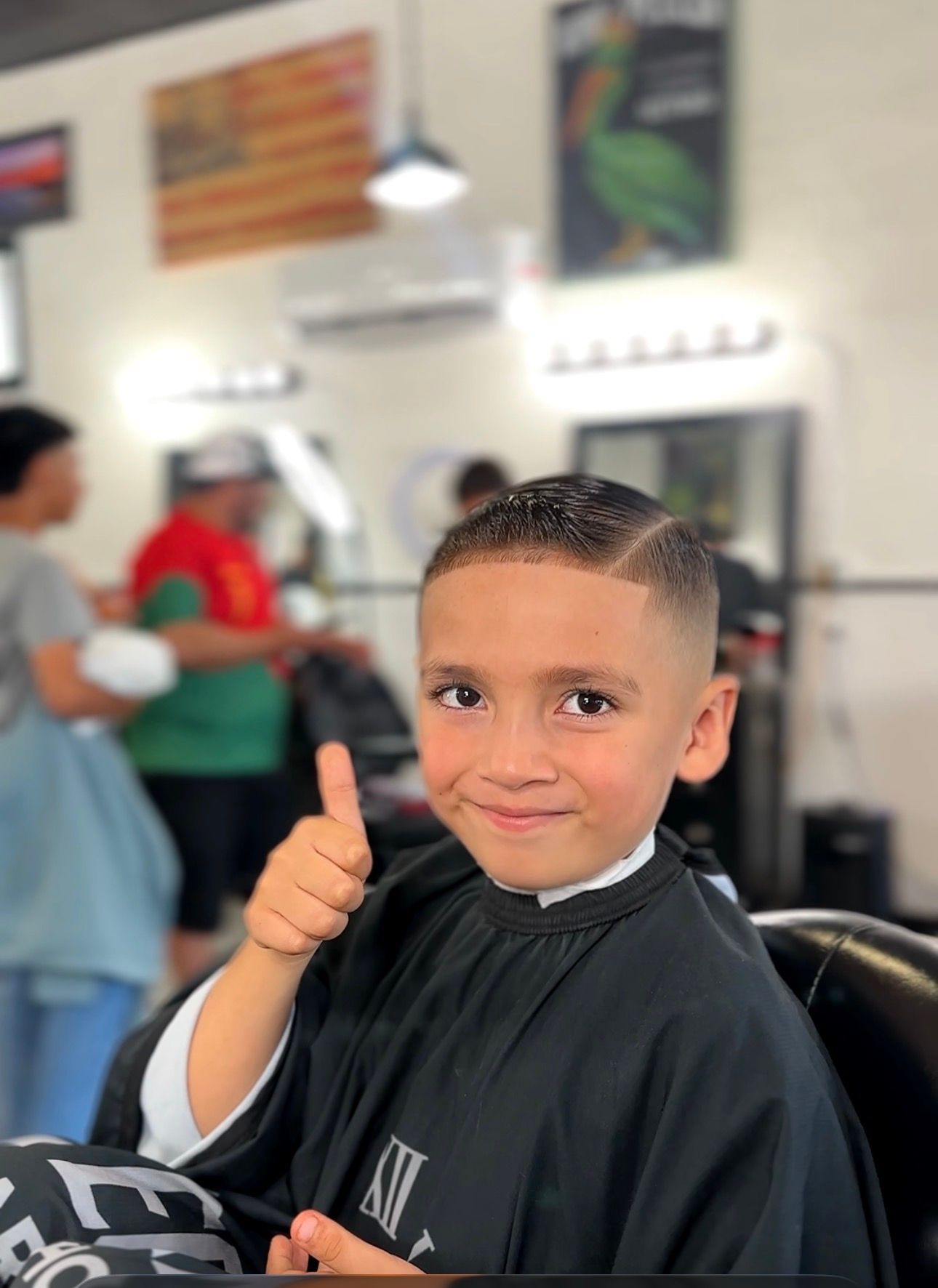 Young boy with a fresh haircut gives a thumbs-up in a barber shop.