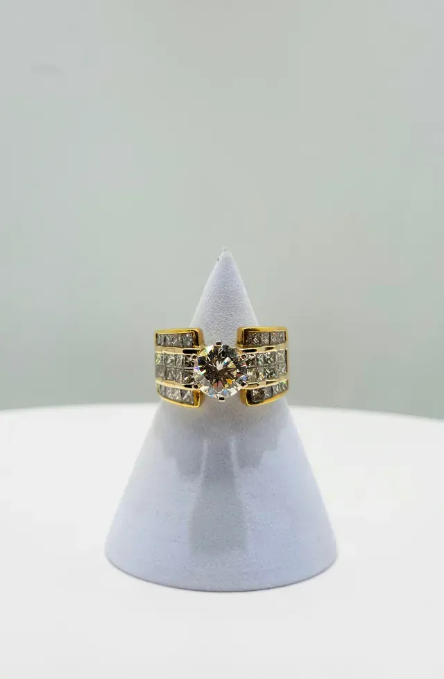 Gold and black ring with dark stones displayed on a gray cone stand against a plain background