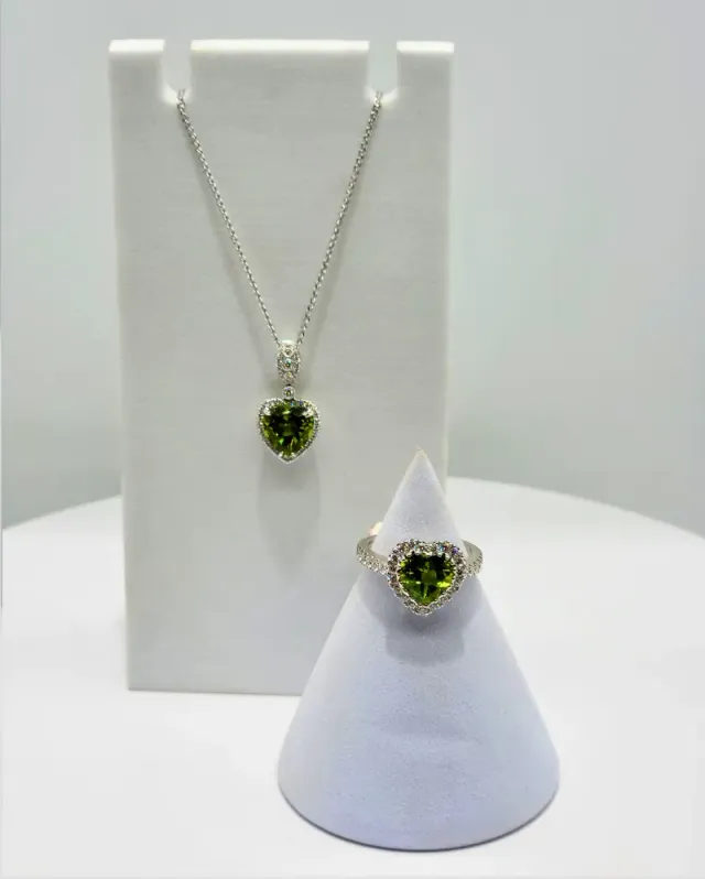 Silver necklace and matching ring with green gemstones displayed on white stands.