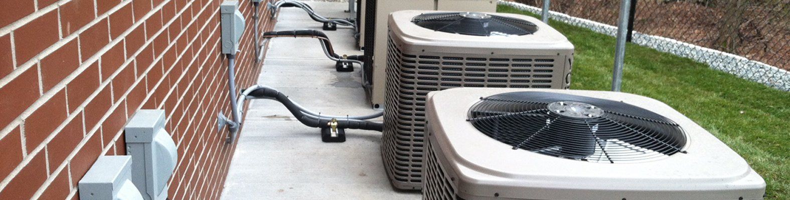 Two air conditioners are sitting on the side of a brick building.