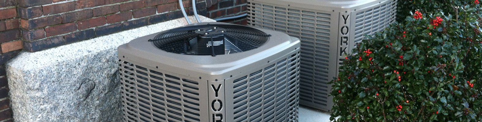 Two air conditioners are sitting next to each other on the side of a building.