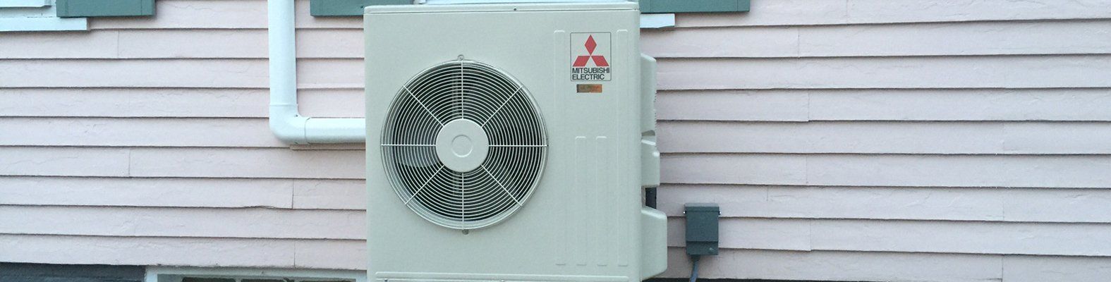 A white air conditioner is mounted on the side of a house.