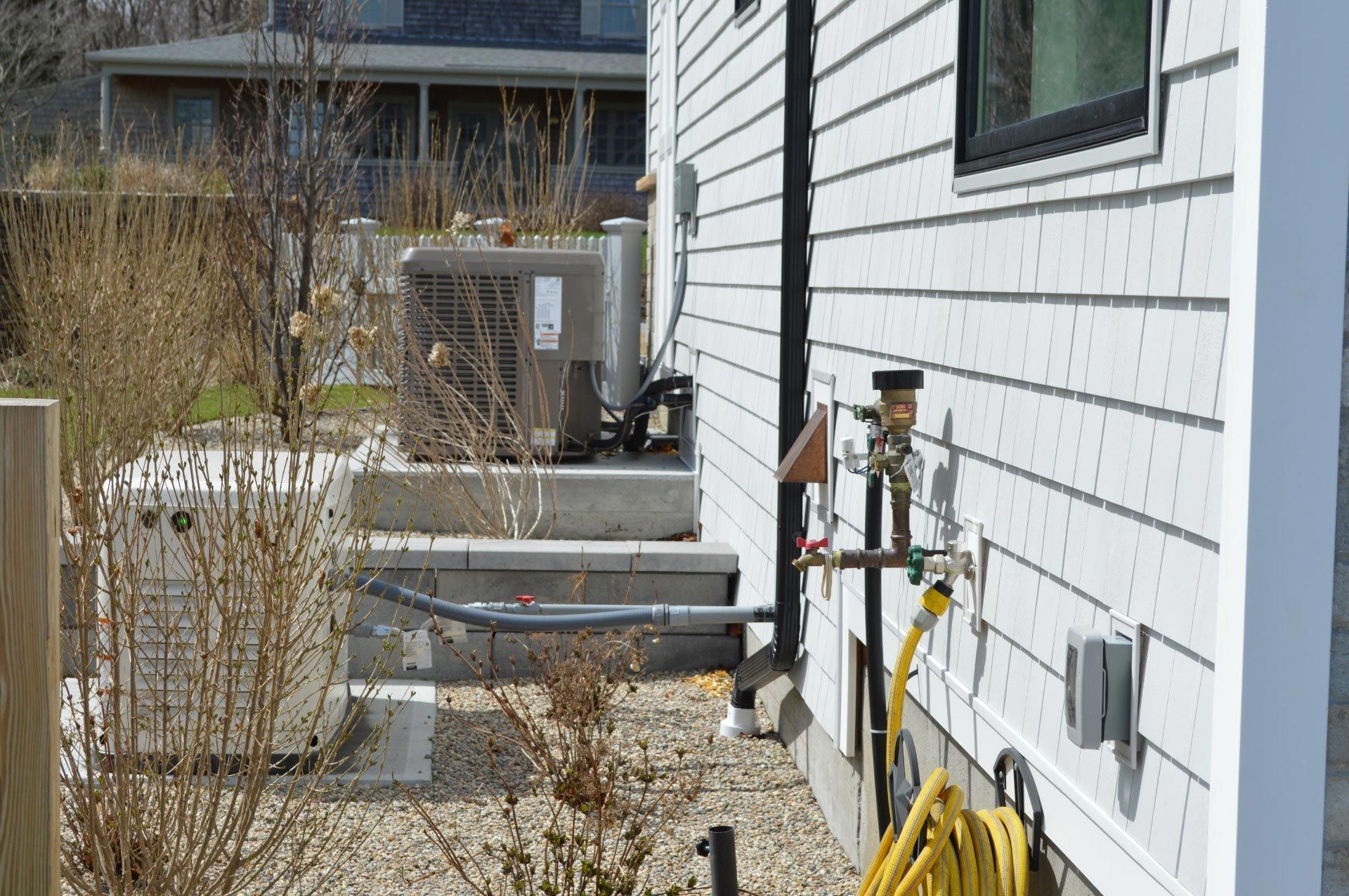 A yellow hose is hanging on the side of a white house.