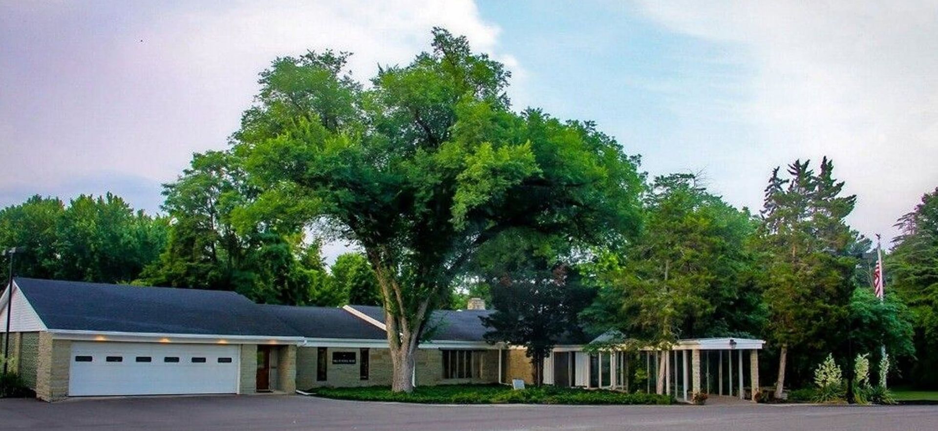 Building with columns and a garage, trees, and sky.