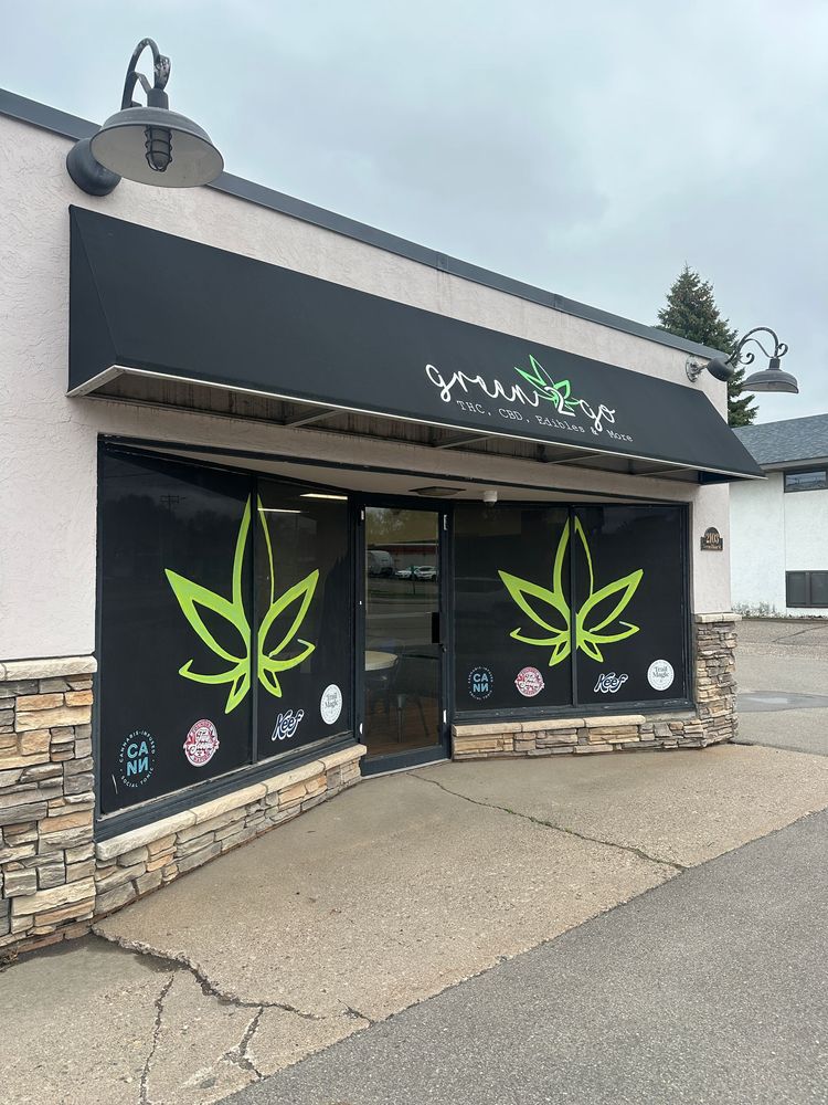 Exterior of a cannabis shop with a black awning and green leaf logos on the windows.