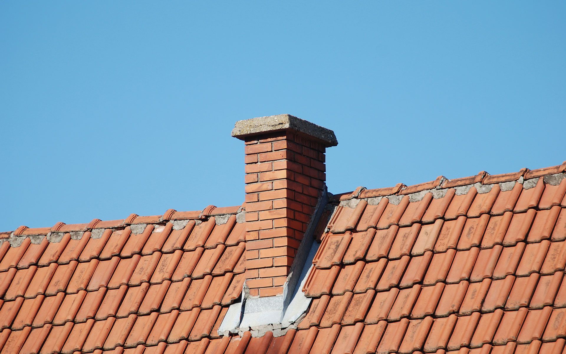 Red brick chimney on red tile roof, against a clear blue sky.