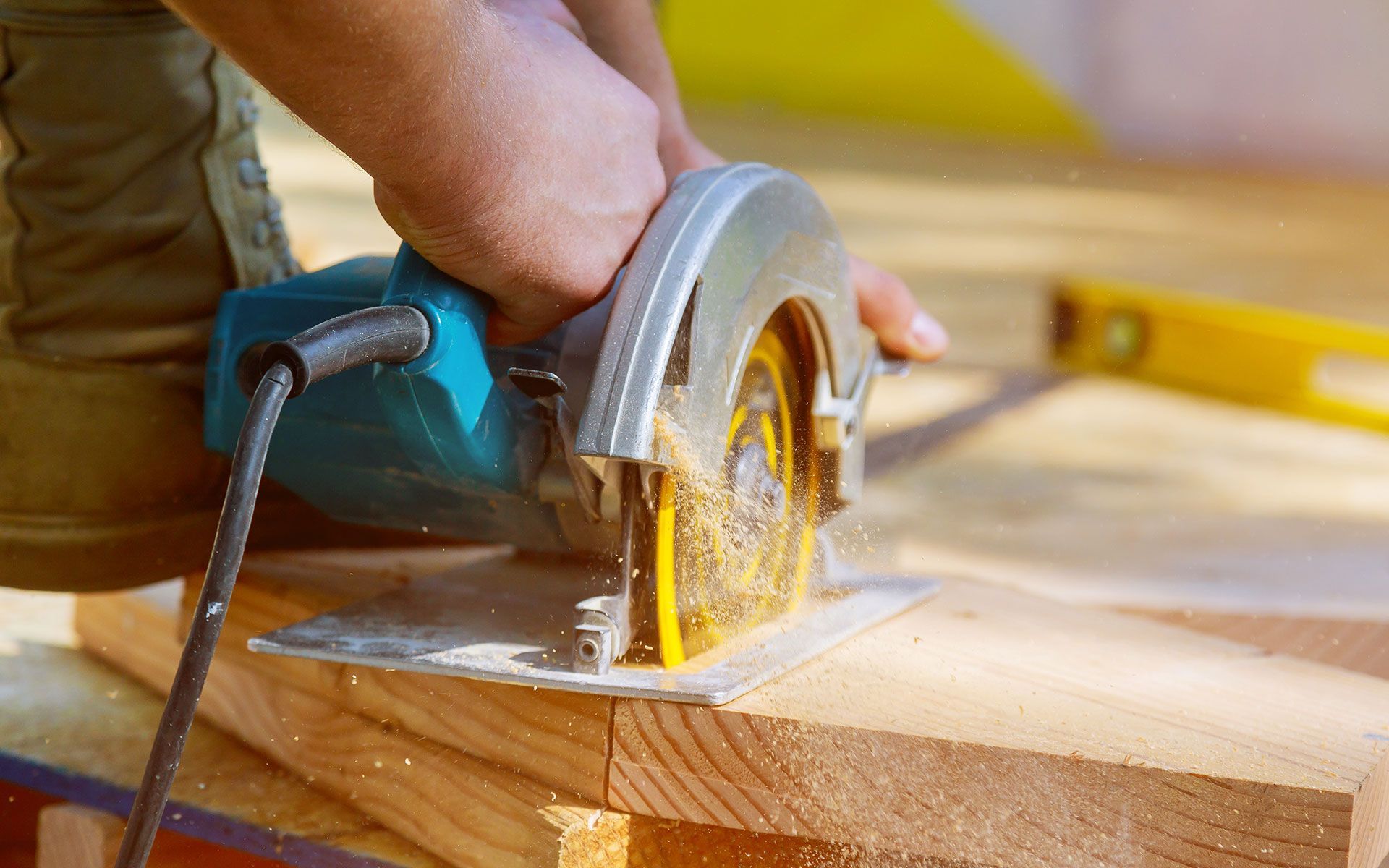 Person using a circular saw to cut wood outdoors; sawdust flying.
