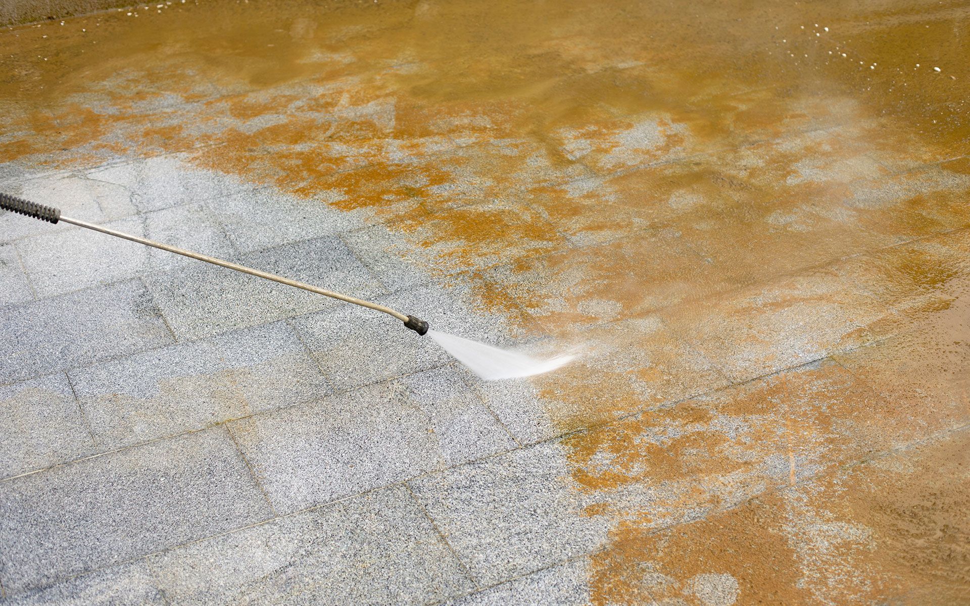 Pressure washing a stone patio, showing a clean strip alongside the dirty section.