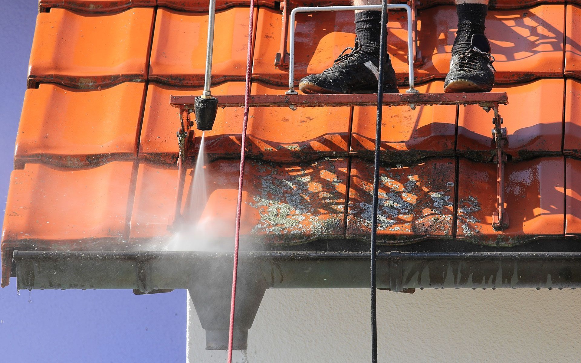 Person on roof using a pressure washer to clean a gutter of algae.