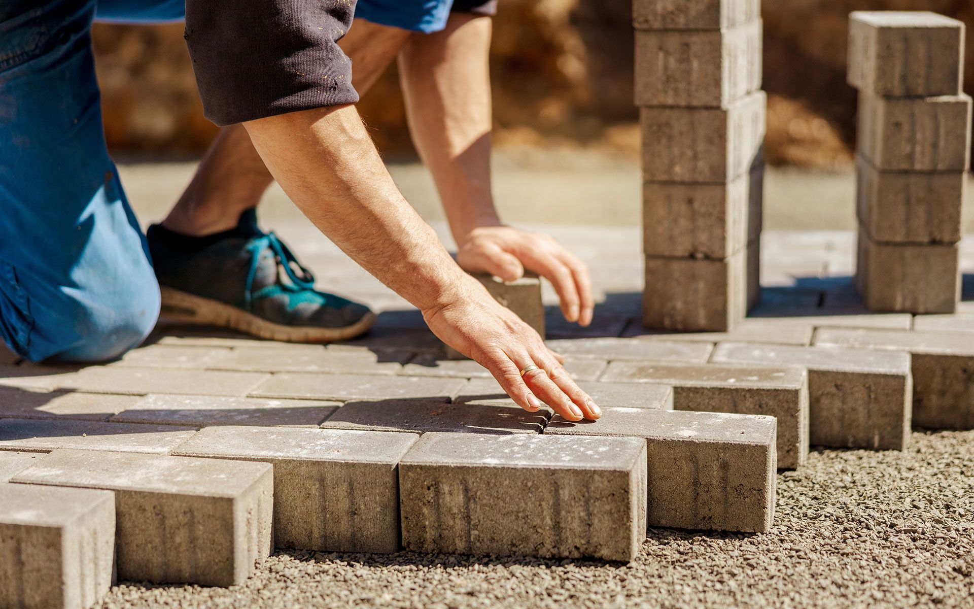 Person laying gray paving stones outdoors.