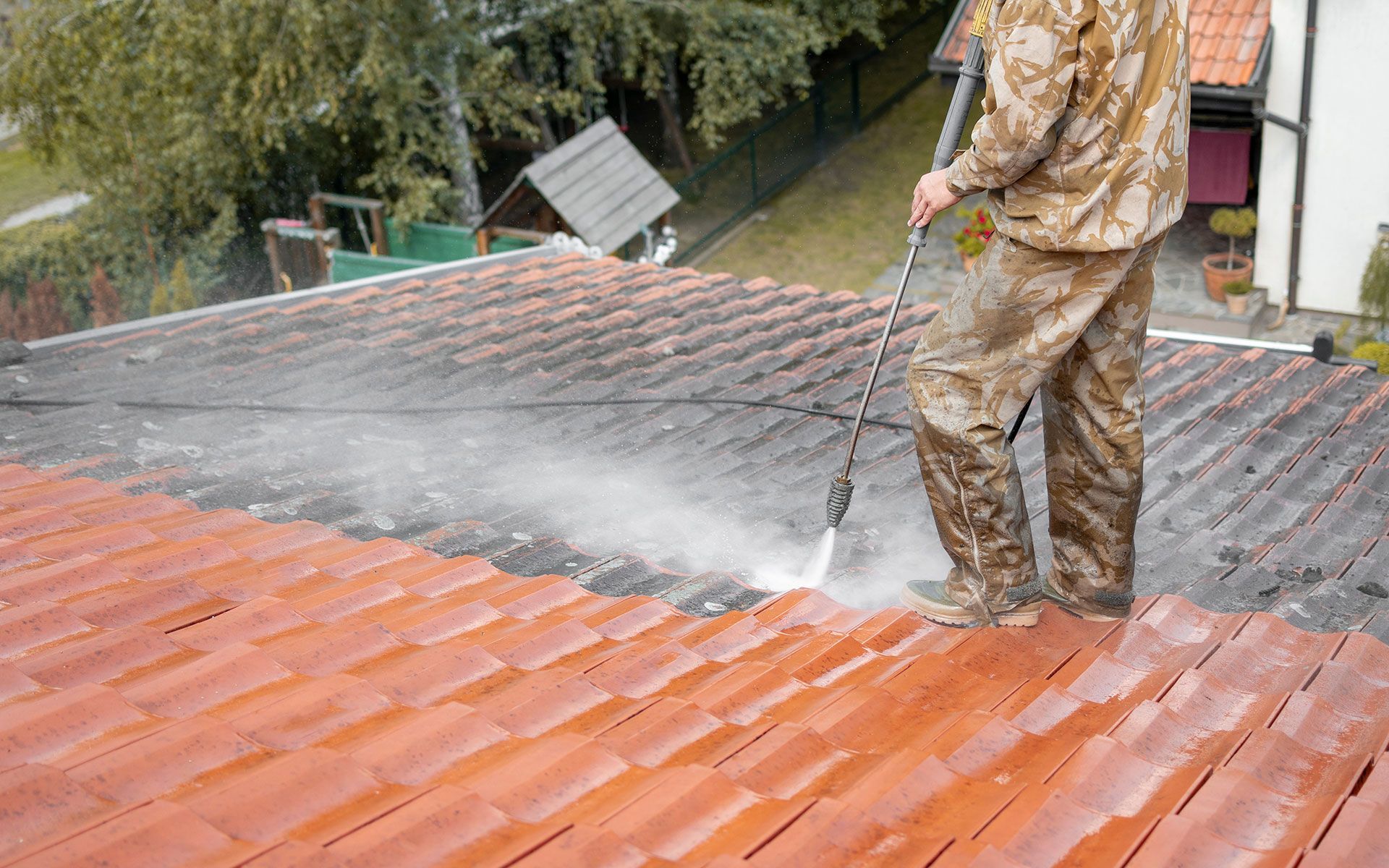 Man pressure washing a red tiled roof, removing dirt and grime.