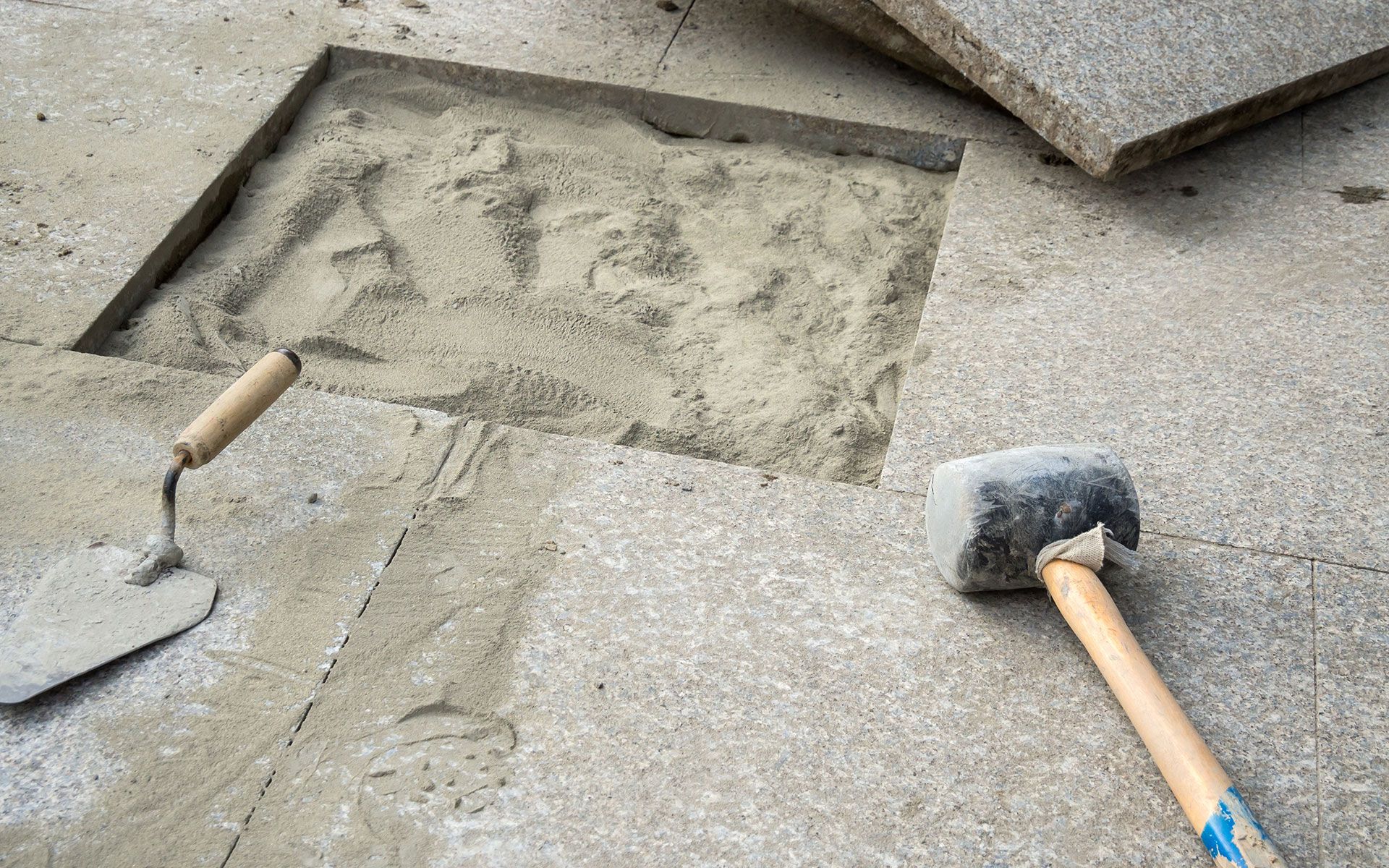 Concrete patio being repaired; hammer and trowel on surface, sand in recessed area.