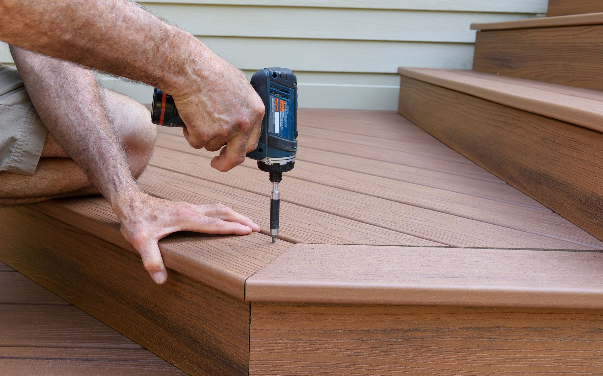 Person using a drill to secure a brown composite deck step to a staircase.