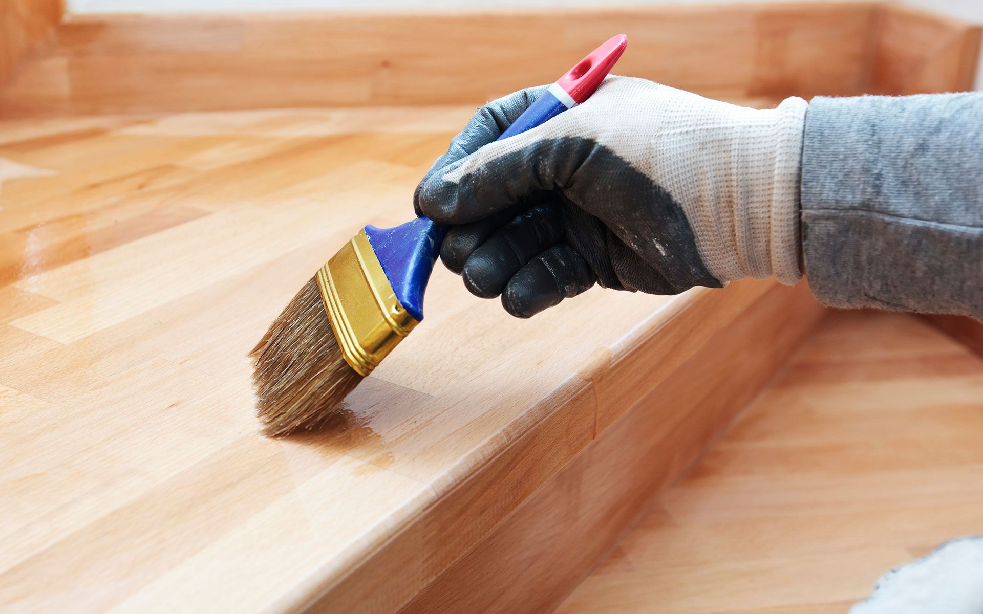 Person varnishing wooden steps with a paintbrush, wearing gloves.