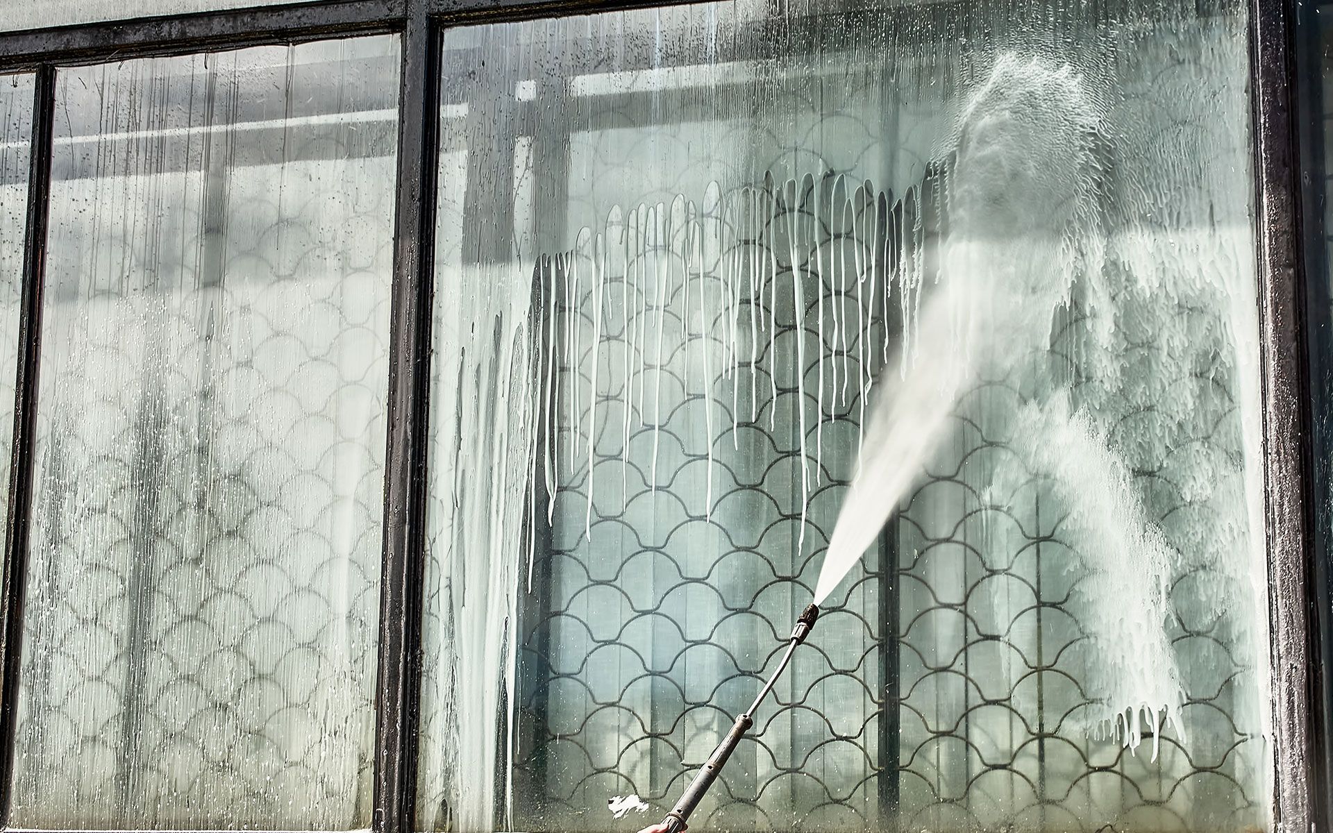 A person sprays a window with a water hose, cleaning the dirty glass.