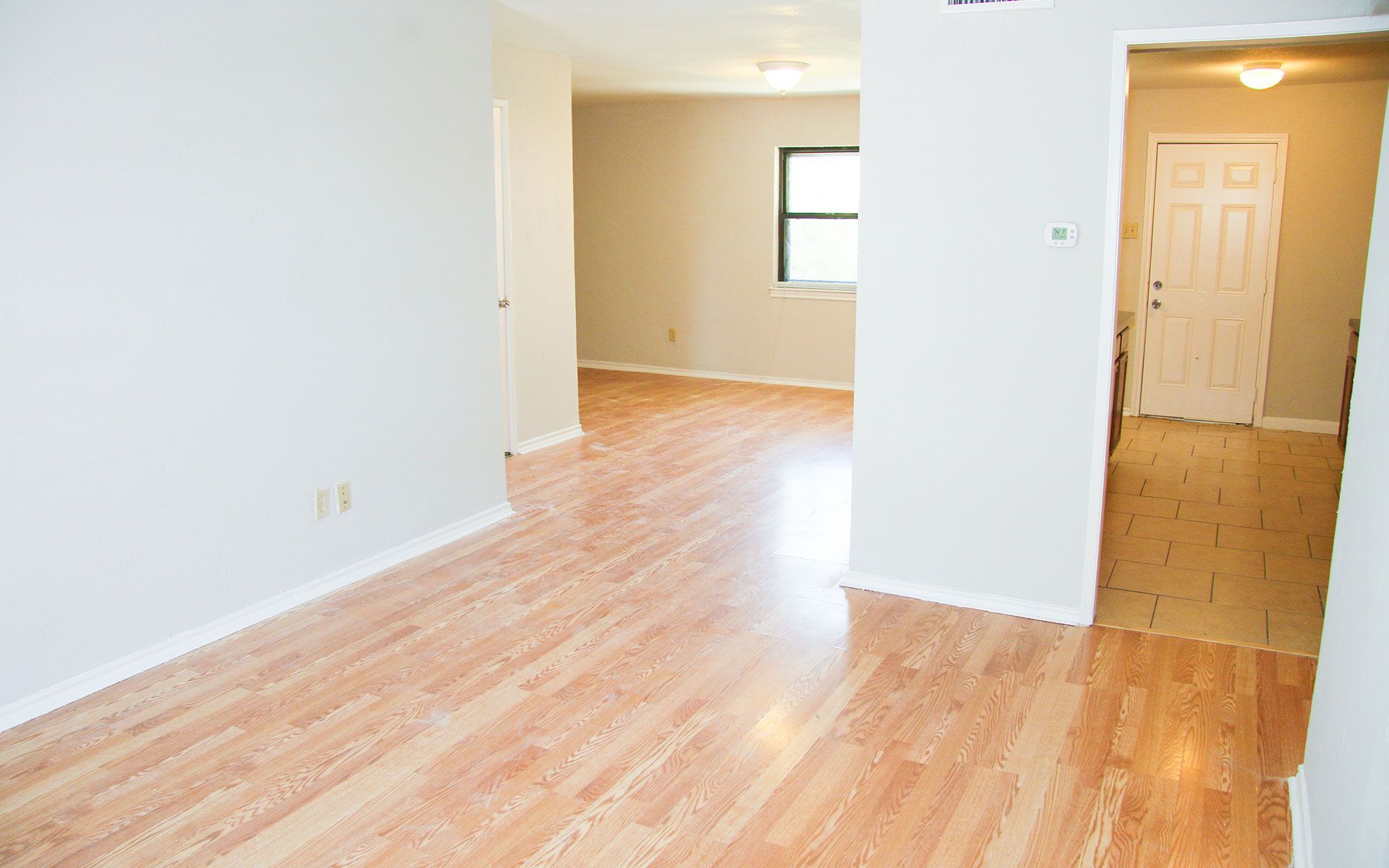Empty apartment interior with hardwood floors, white walls, and doorway.