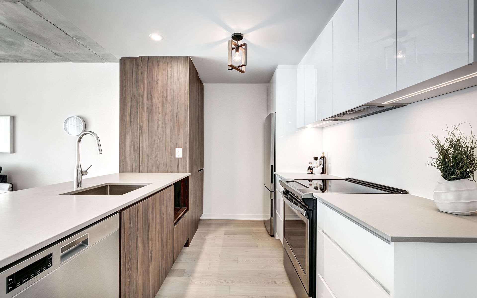 Modern kitchen with white countertops, wood cabinets, stainless steel appliances, and light wood flooring.