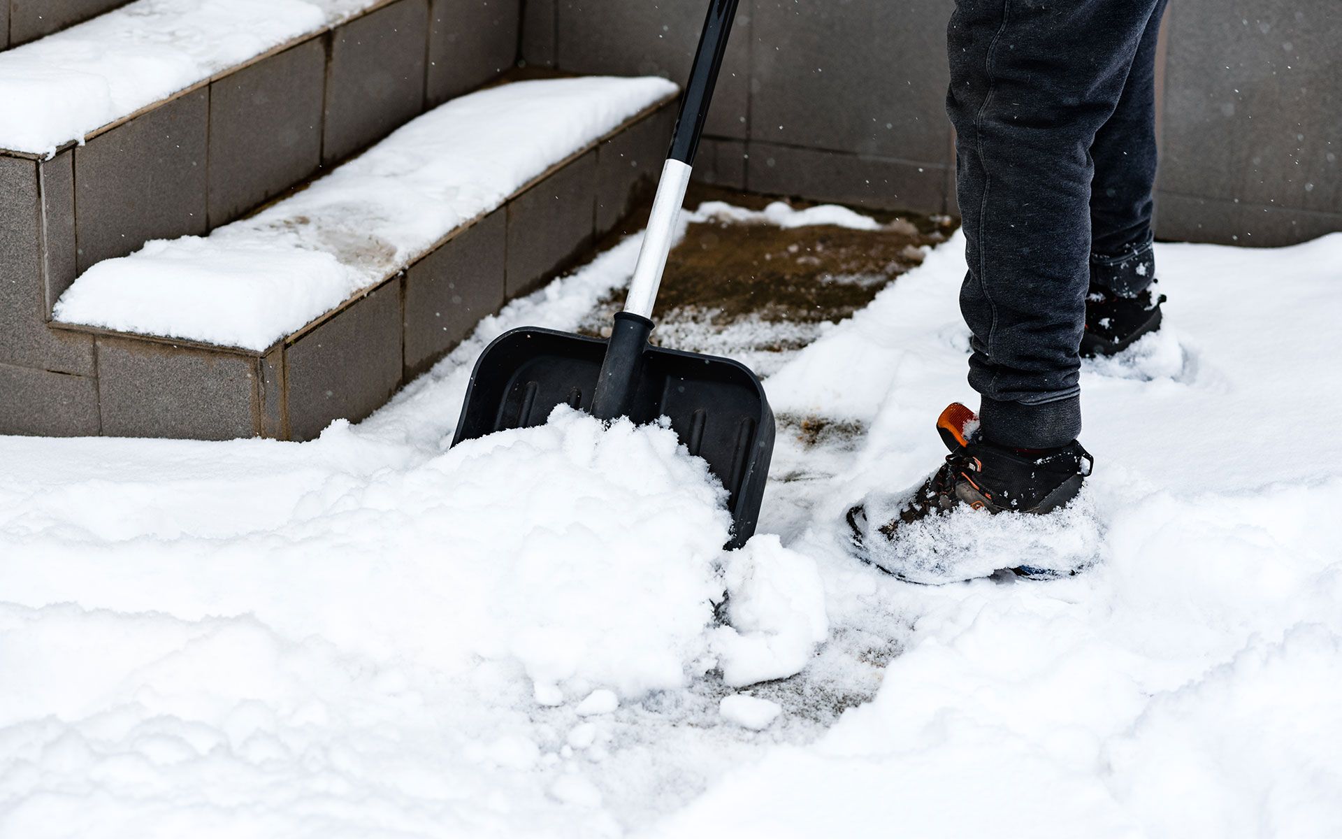 Person shoveling snow from a walkway, near steps.