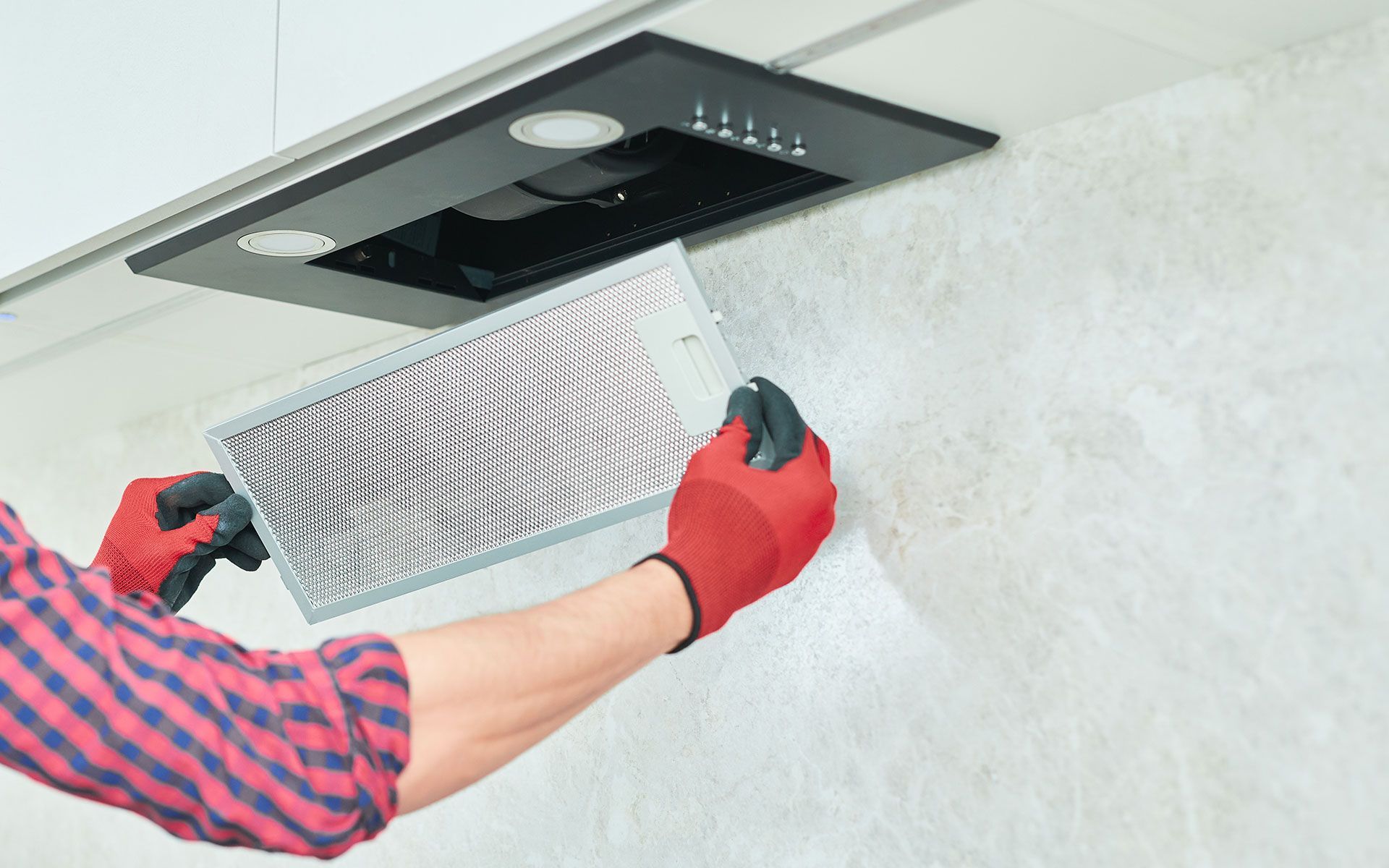 Person in red gloves replacing a range hood filter in a kitchen.