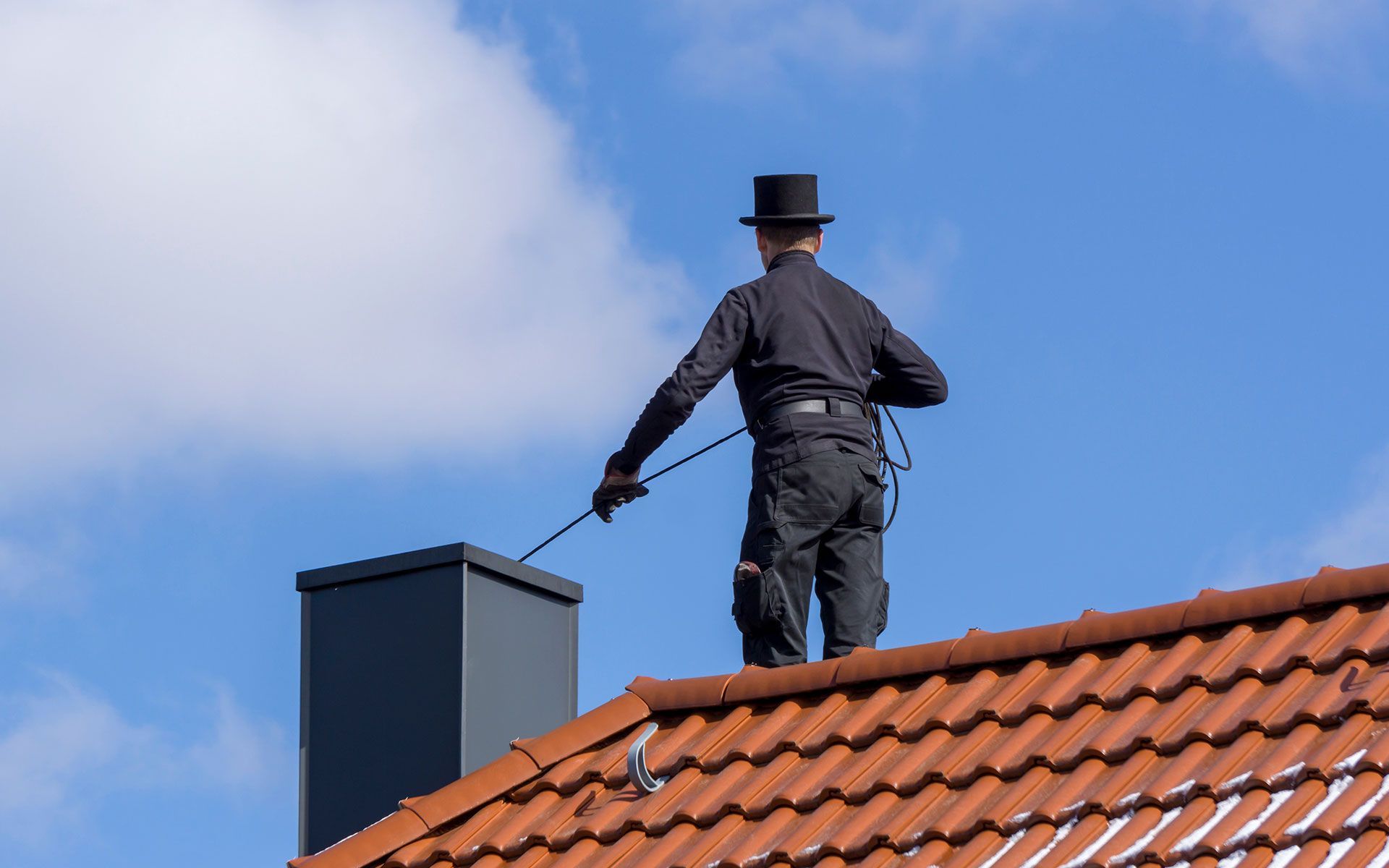 A chimney sweep in a top hat on a roof cleaning a chimney against a blue sky.