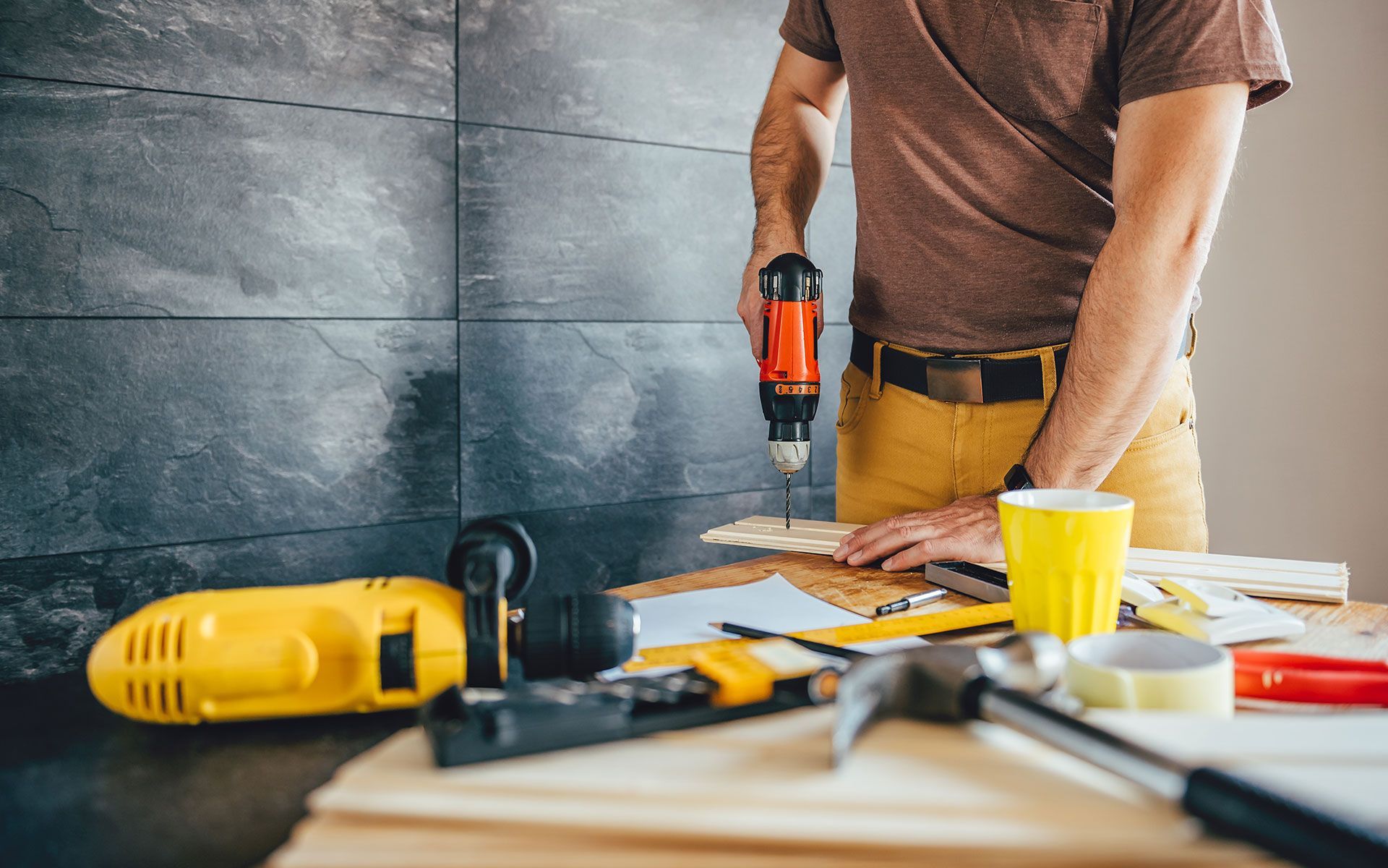 A person using a drill on wood, tools on a table.