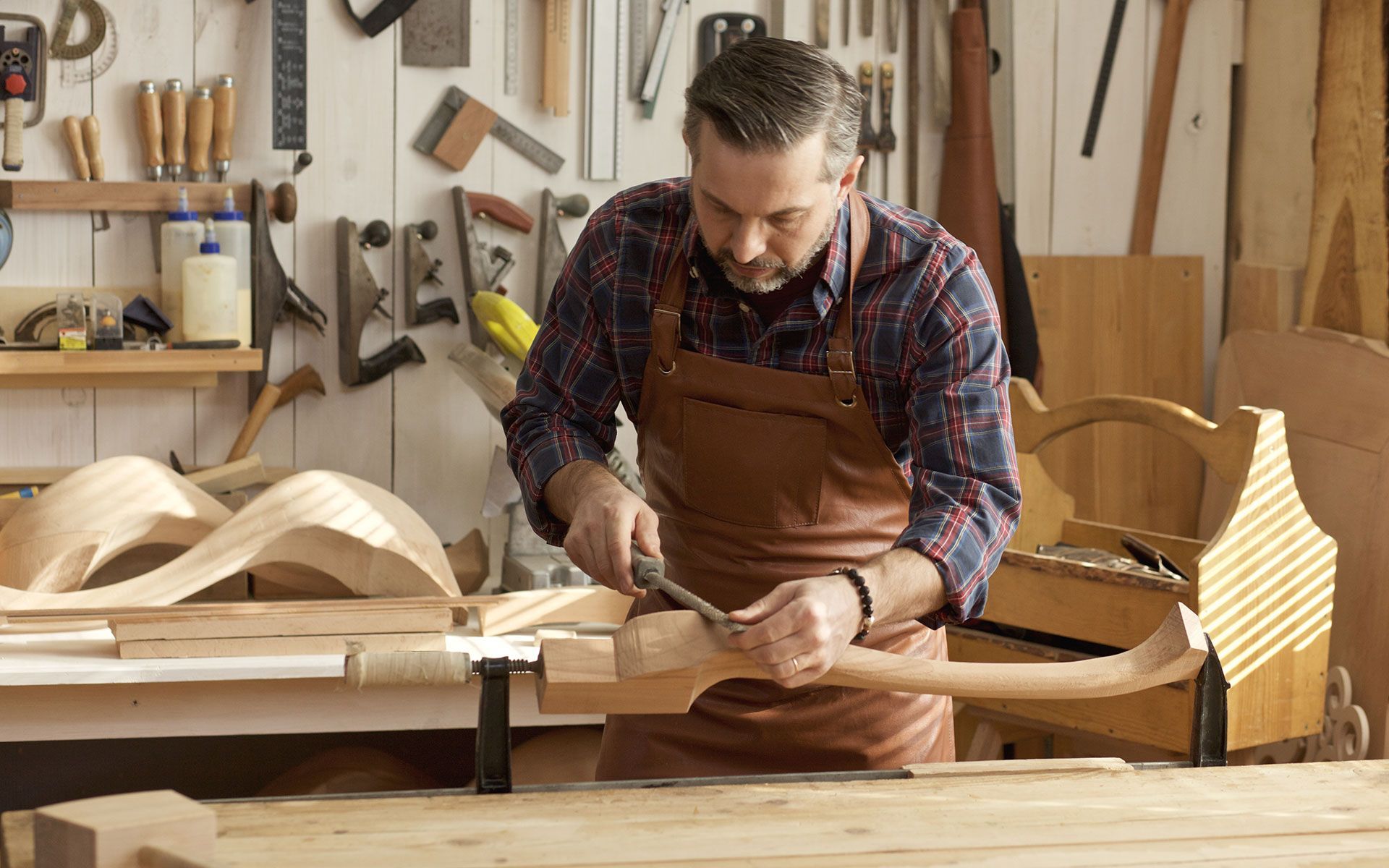 A craftsman carves wood in his workshop, wearing a leather apron.