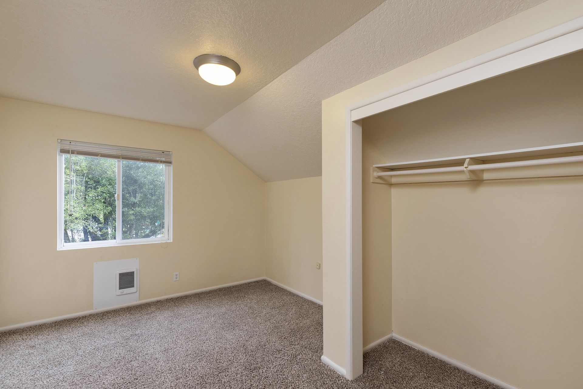 An empty bedroom with a closet and a window.