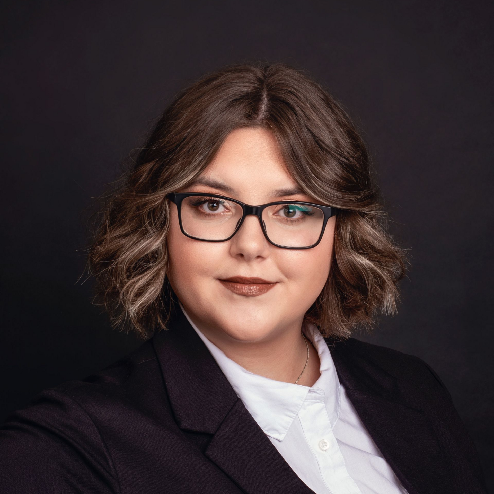 Woman with glasses, in a suit, looking at the camera with a neutral expression.