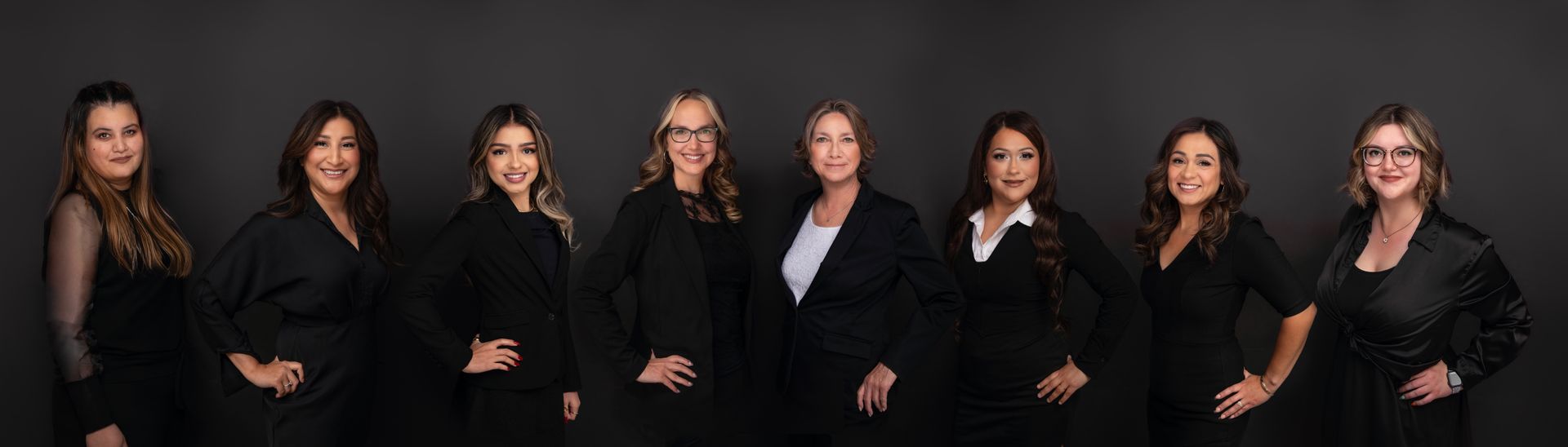 Group of professional women in suits, hands on hips, against a dark background.