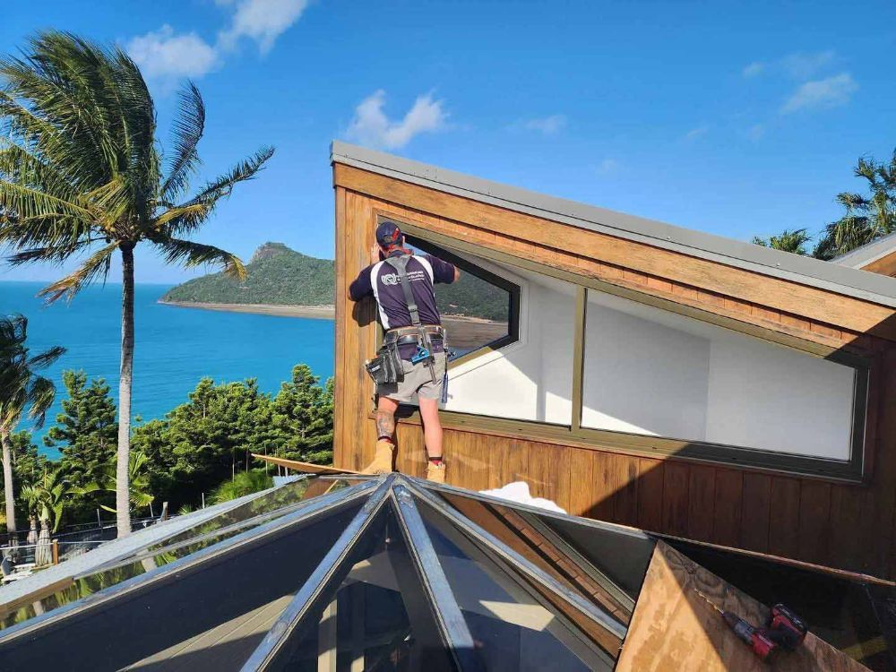 A Man Is Standing on The Roof of A Building Overlooking the Ocean — North Queensland Glass & Glazing In Cannonvale, QLD