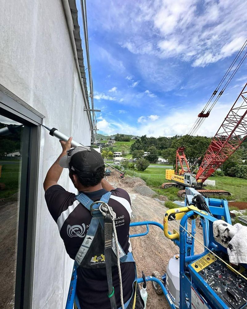 A Man Is Working on A Building with A Crane in The Background — North Queensland Glass & Glazing In Cannonvale, QLD