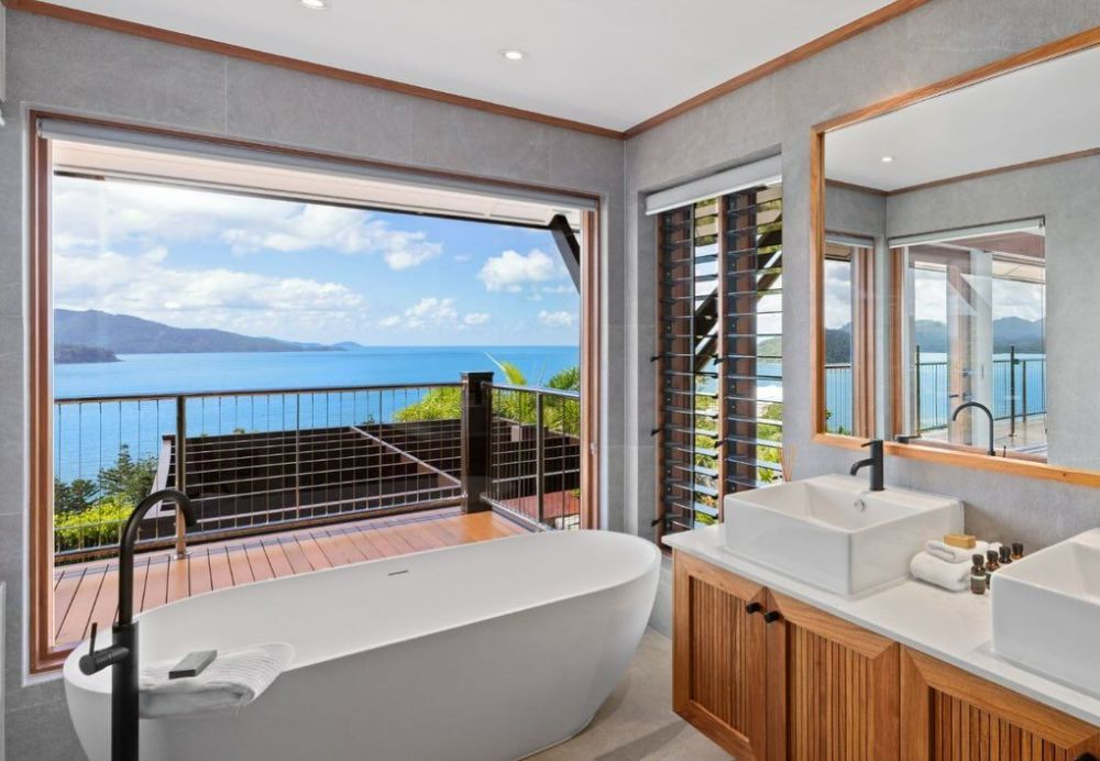 A Bathroom with A Bathtub, Sink, and Mirror with A View of The Ocean — North Queensland Glass & Glazing In Cannonvale, QLD