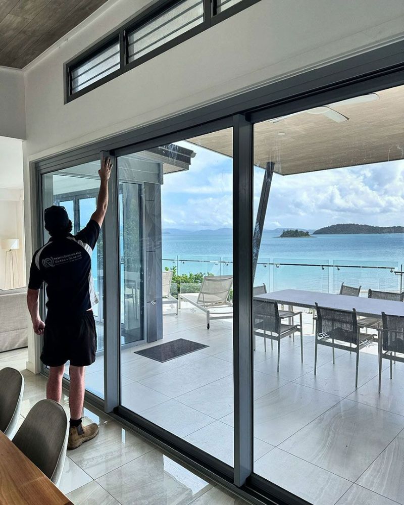 A Man Is Cleaning a Sliding Glass Door in A Living Room — North Queensland Glass & Glazing In Cannonvale, QLD