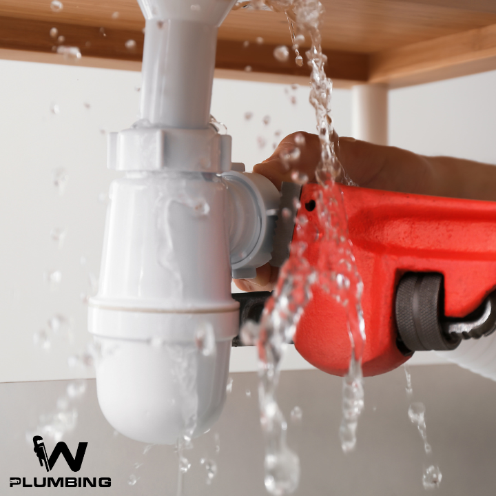 A person is fixing a sink pipe with a plumbing logo in the corner