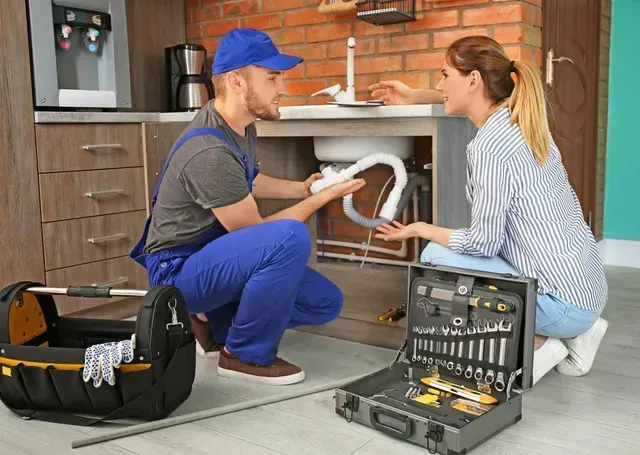 plumber in Westminster, CO talking to resident while fixing sink in home. 