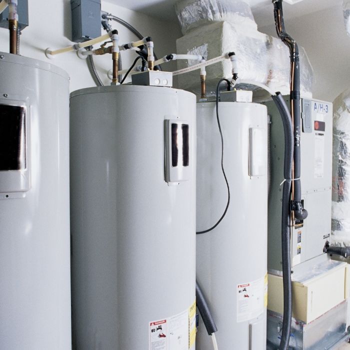 Three grey commercial water heaters connected with piping inside a mechanical utility room.