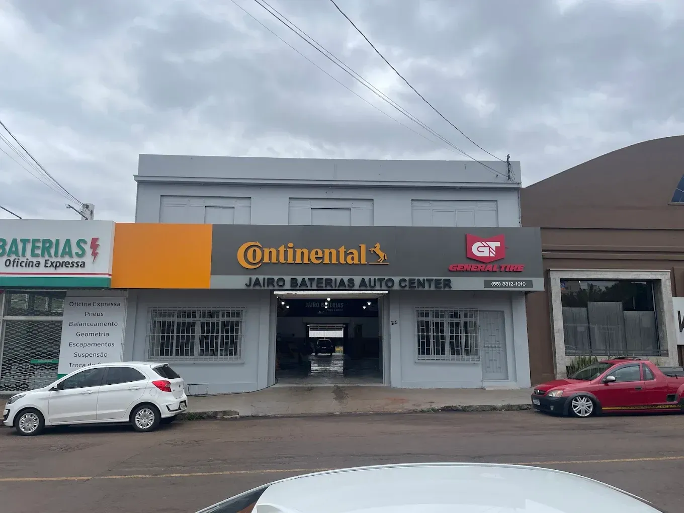 Um homem de macacão amarelo segura um pneu na frente de um carro.
